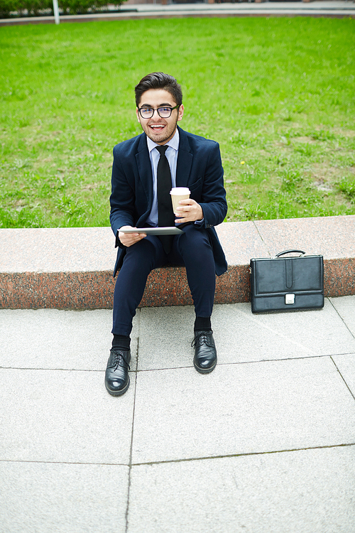 Successful salesman with drink and tablet expressing happiness of new business deal