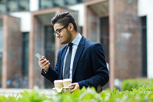 Businessman with drinks and smartphone texting outdoors