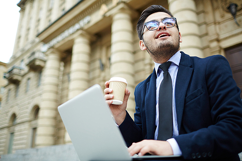 modern broker with hot drink and laptop working in urban