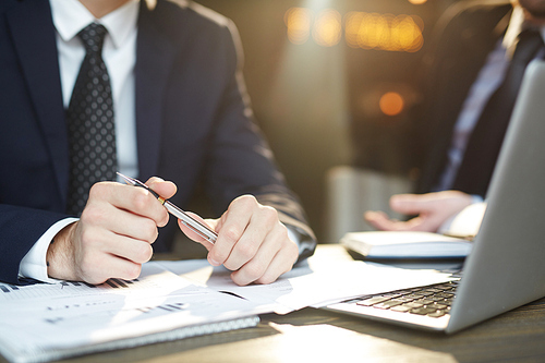 Closeup portrait of two unrecognizable successful business partners wearing black formal suits reviewing statistics documents and discussing deal at table during meeting