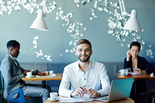 Young successful economist working with papers while sitting in cafe