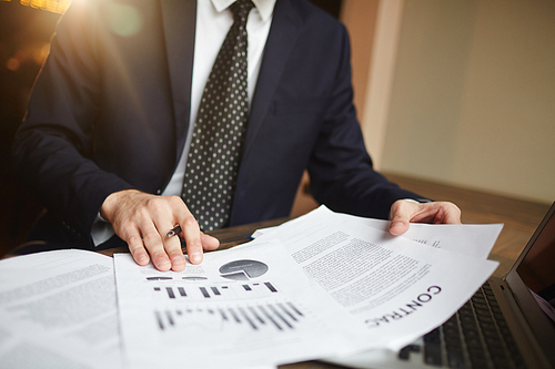 Closeup portrait of unrecognizable successful businessman reviewing finance statistics and contract paperwork at desk with laptop