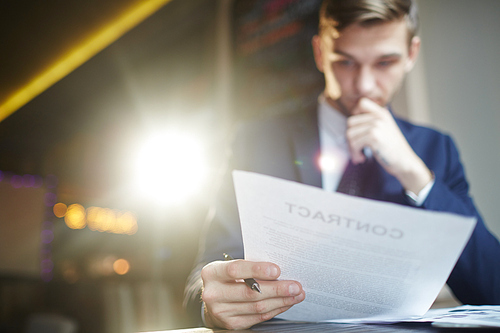 Portrait of young successful businessman reading contract documents at desk, busy with paperwork, focused