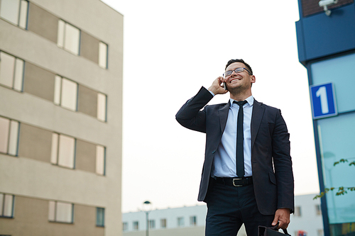 Modern businessman speaking by smartphone outdoors