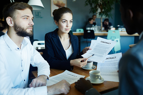 Portrait of three business people sitting at table during meeting in cafe: beautiful businesswoman holding contract and explaining the deal to partners