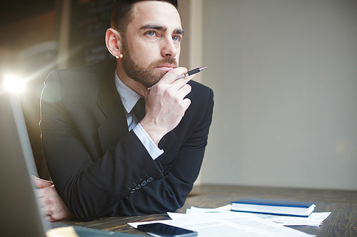 Portrait of modern successful businessman wearing black formal suit working in office with documentation, resting head on hand thinking and looking away