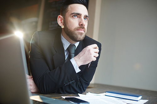 Portrait of modern successful businessman working in office, thinking and looking away