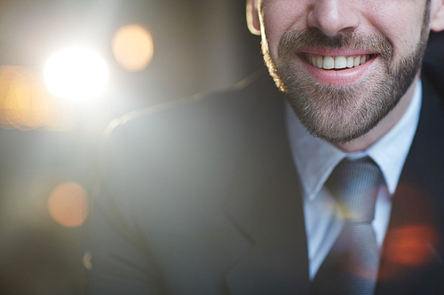 Closeup midsection shot of modern unrecognizable bearded businessman smiling joyfully to camera against black background with lens flare