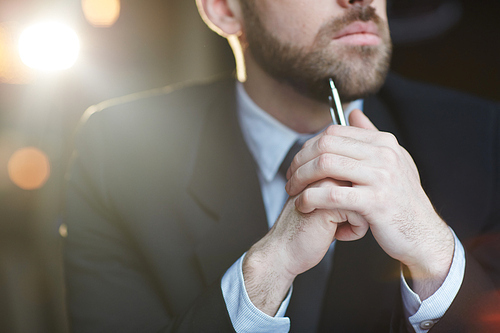 Closeup midsection shot of modern unrecognizable bearded businessman thinking and looking away against black background with lens flare