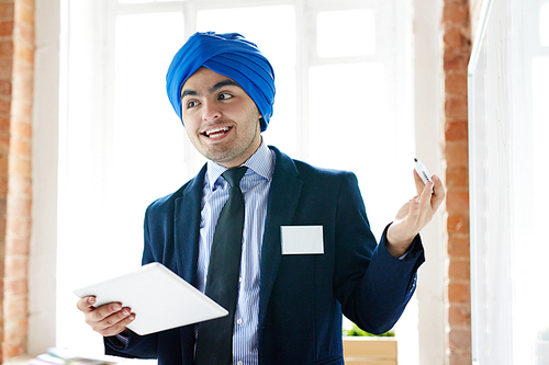 Arabian businessman with highlighter and tablet explaining something on whiteboard