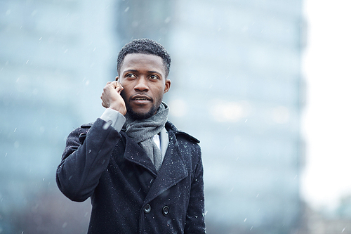 Portrait of handsome African -American businessman speaking on phone in snowy autumn city street, looking away