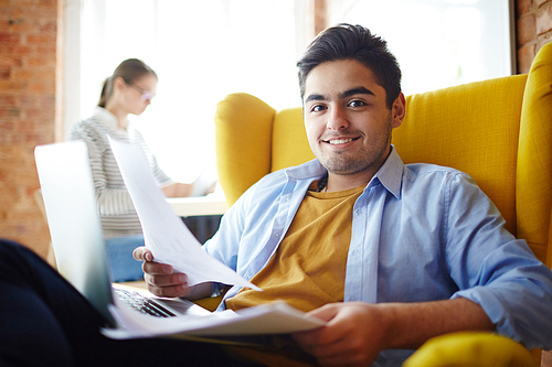 Young employee with paper and laptop sitting in armchair