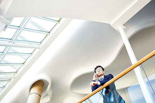 Lawyer with cellphone leaning on banister inside modern business center