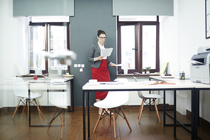 Young businesswoman reading financial papers by wall of offfice