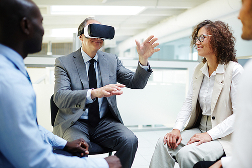Mature business leader in vr goggles telling his subordinates what he sees in another reality