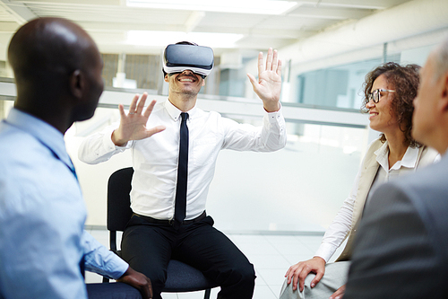 Happy businessman with vr goggles sitting among his colleagues looking at him