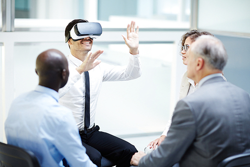 Happy businessman watching curious video in vr headset with colleagues near by