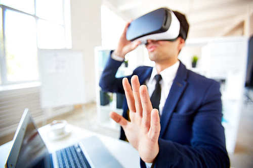 Modern employee with vr headset enjoying augmented reality by workplace