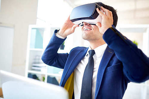Contemporary businessman with 3d goggles watching curious game or video by workplace