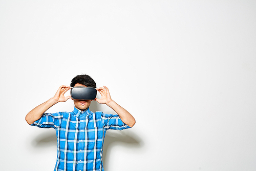 Stylish young man wearing virtual reality headset playing exciting game while standing against white background