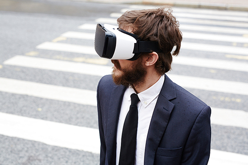 Contemporary businessman with virtual reality goggles crossing street