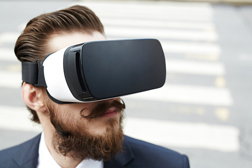 Young businessman with beard and moustache wearing vr goggles in the street