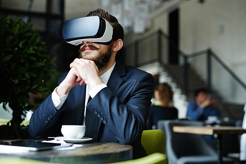 Businessman with virtual reality headset enjoying video while spending time in cafe after work