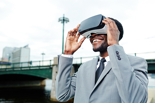 Happy man in suit and vr headset looking through virtual life while standing by riverside