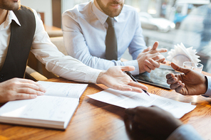 Close-up view of confident bearded businessmen in suits sitting at wooden table near window and discussing new contract terms before signing it.