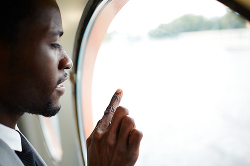 Profile view of pensive African American man enjoying picturesque view from window of ship cabin, head and shoulders portrait