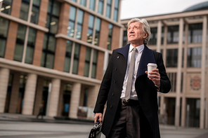 Senior businessman with briefcase and plastic glass with hot drink hurrying for work in the morning