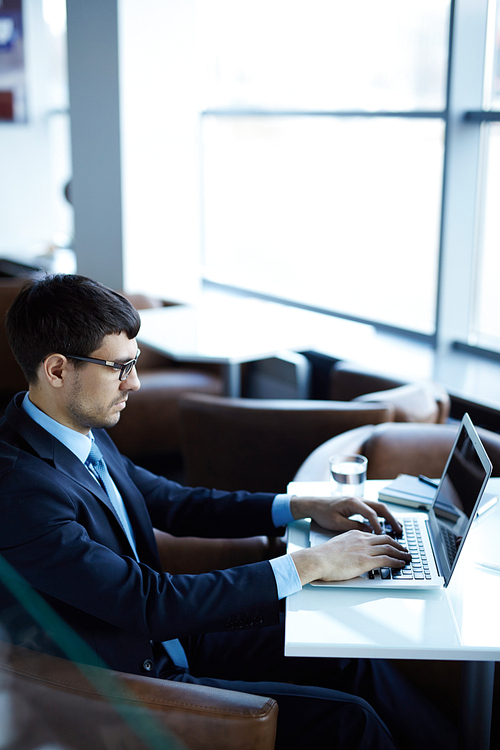 Portrait of young bearded financial manager sitting in office lobby and preparing annual accounting reports, profile view