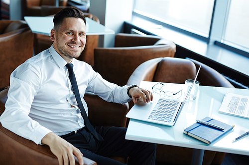 Stylish middle-aged businessman  with toothy smile while working on project in cozy small cafe, waist-up portrait