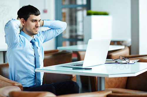 Tired handsome financial manager putting hands on nape and searching mistake in his calculations on laptop, waist-up portrait