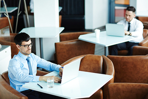 High angle view of confident businessmen wrapped up in work while sitting in cozy small cyber cafe, waist-up portrait