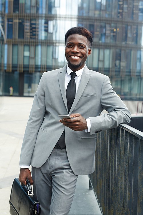 Happy young agent with briefcase and smartphone  in urban environment