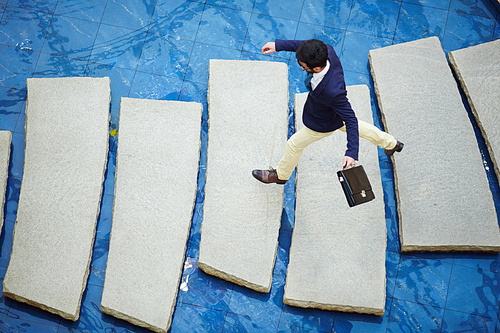 Above view shot of modern businessman with briefcase stepping over obstacle tiles on blue global world background