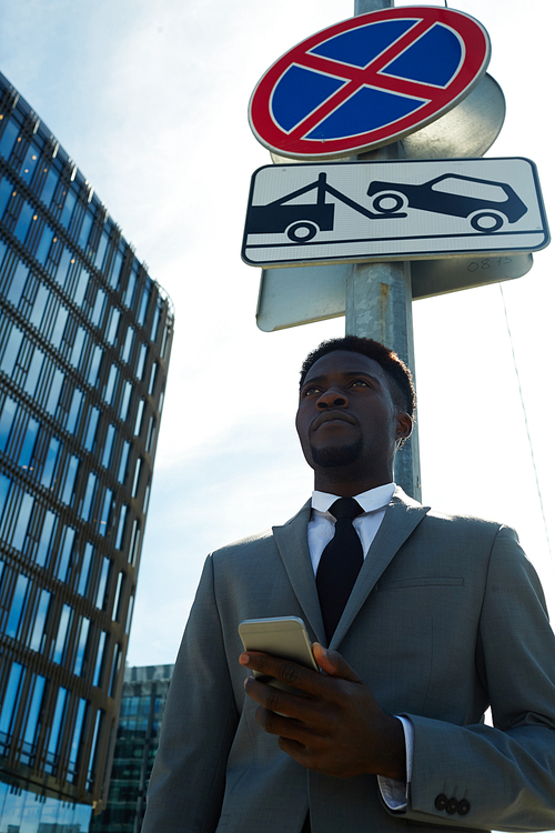 African-american manager with smartphone waiting for taxi by evacuation sign