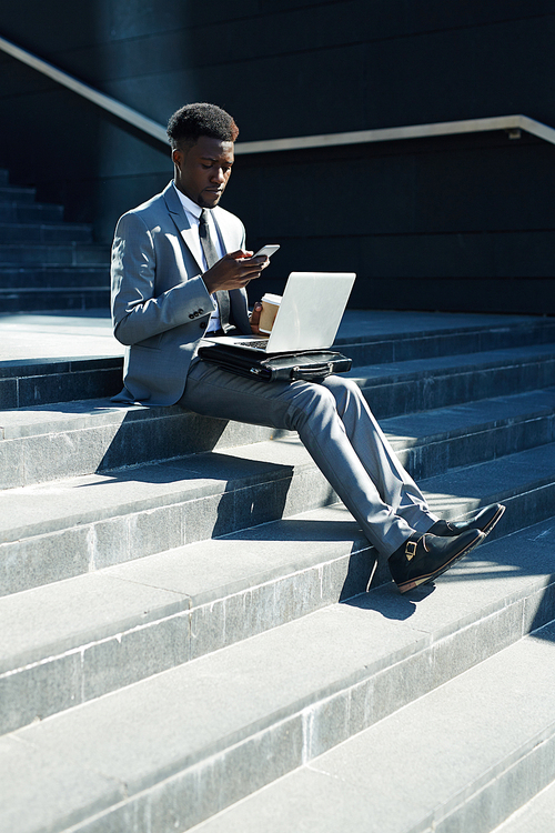 Mobile entrepreneur with laptop and smartphone messaging on stairs