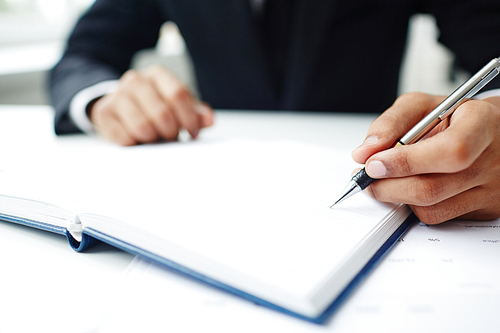 Close-up shot of unrecognizable entrepreneur wearing suit sitting at office desk and taking necessary notes while preparing for important business meeting