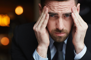 Portrait of modern bearded businessman , rubbing his temples stressed and troubled against black background