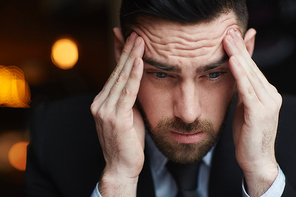 Portrait of frustrated bearded businessman rubbing his temples ooking stressed and troubled against black background