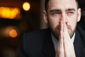 Portrait of modern bearded businessman looking away with red teary eyes, stressed and tired against black background, covering his mouth with hands