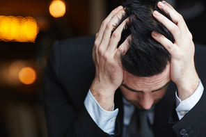 Portrait of modern businessman clasping head with hands, fighting stress and exhaustion against black background