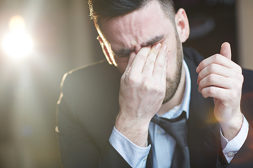 Portrait of tired adult man rubbing eyes and crying against black background with lens flare