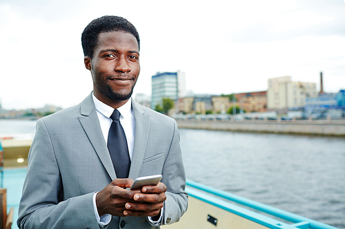 Portrait of smiling African American manager  while using smartphone and enjoying picturesque view from upper deck of ship
