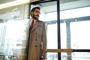 Stylish businessman in beige trench-coat, suit and red tie just entered cafe to for drink or lunch