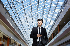 Serious agent with smartphone in modern office center