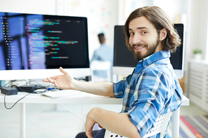 Young successful specialist in data decoding sitting by workplace and pointing at computer monitor