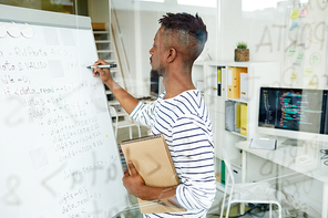 Young trainee with notepad writing down software codes on whiteboard in office